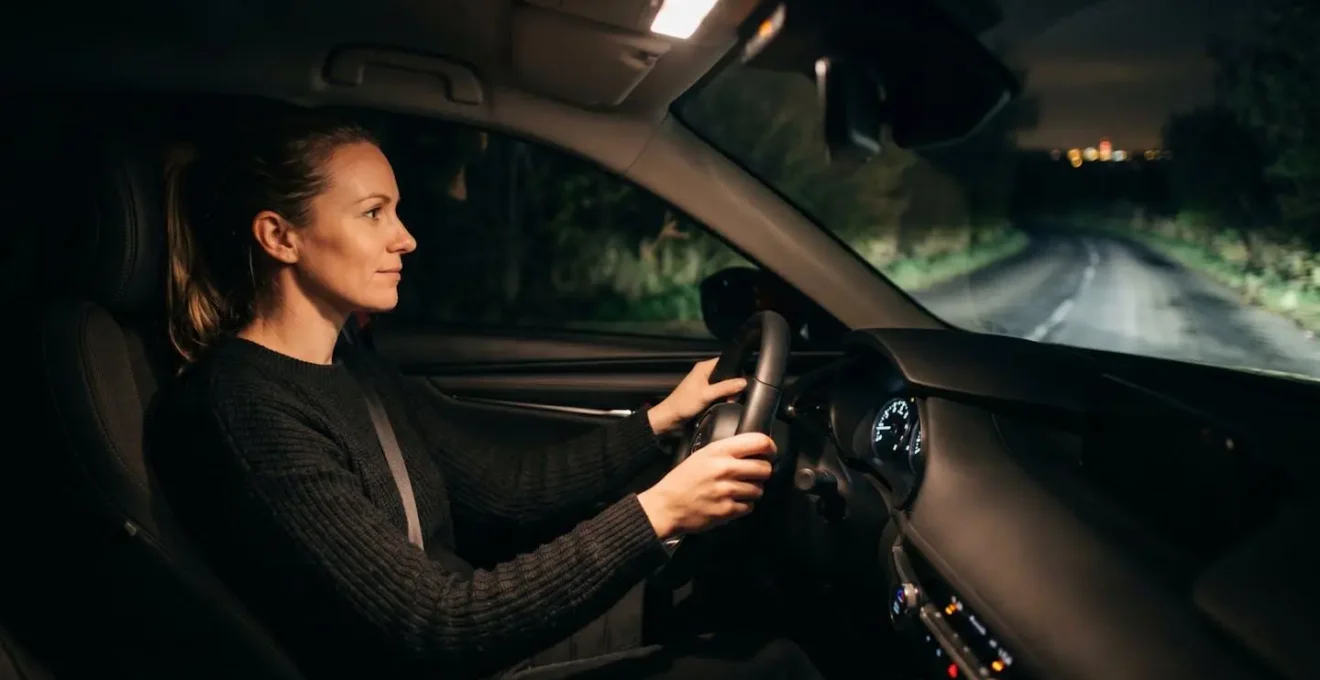 Femme au volant la nuit sur une route de campagne, éclairée par les phares de sa voiture