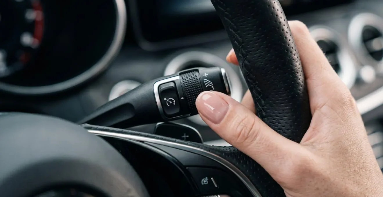 Gros plan sur une main de femme activant le limiteur de vitesse au volant dans un contexte urbain.
